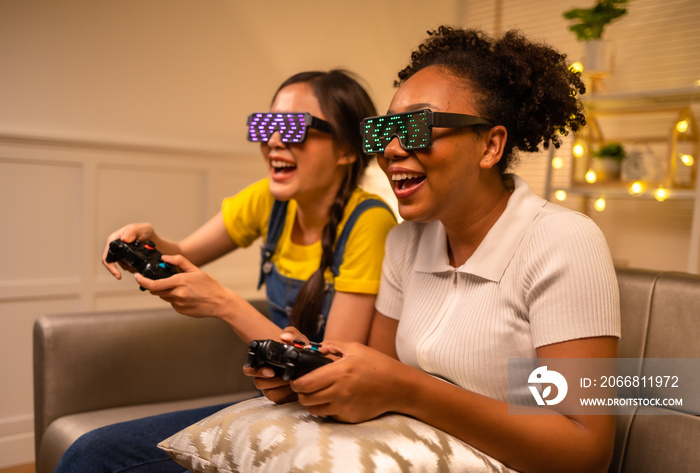 Young  asian and african woman playing video games at home living room at night.Lesbian couples or lgbt activities on vacation inside the room.