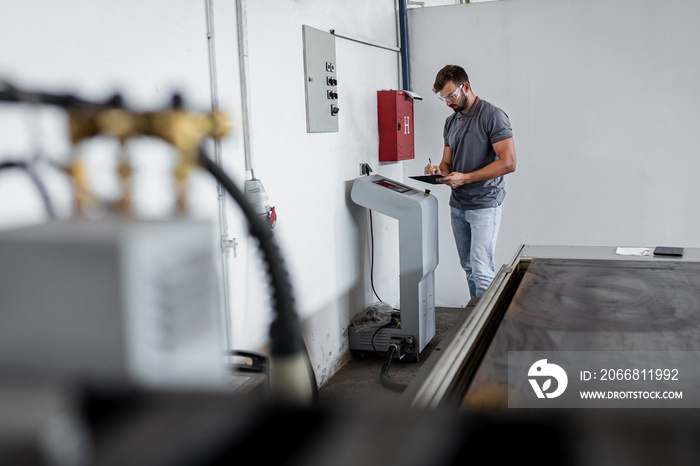 Young engineer setup plasma cutter for work in metalwork workshop.