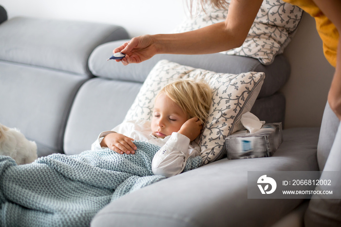 Sick child, toddler boy lying on the couch with his white puppy in living room with fever, resting