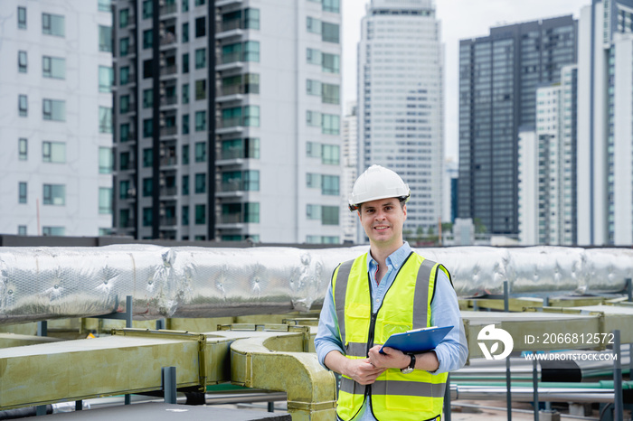 An engineer’s portrait is examining the cooling tower air conditioner of a huge industrial building to control airflow.