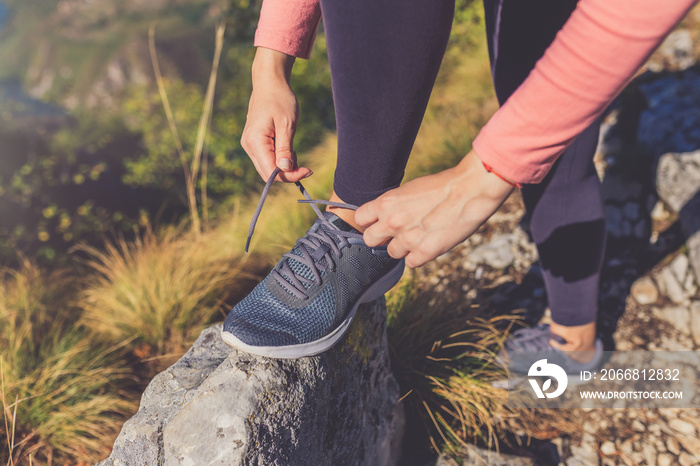 Sporty active woman in sportswear kneeling on rock and tying shoelaces. Morning training in nature.