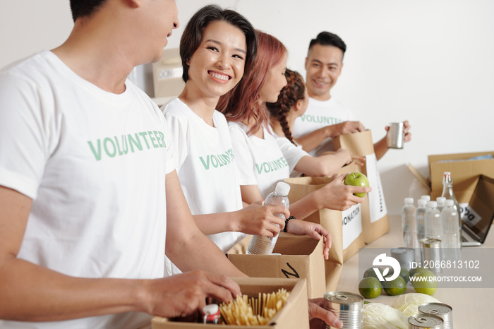 Group of smiling young students volunteering at charitable foundation office and packing food and waterr in big paper packages for people in need