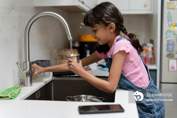 Little girl pouring water from faucet into mug