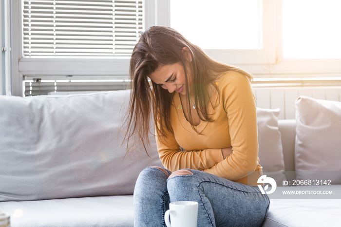 Woman lying on sofa looking sick in the living room. Beautiful young woman lying on bed and holding hands on her stomach. Woman having painful stomachache on bed, Menstrual period