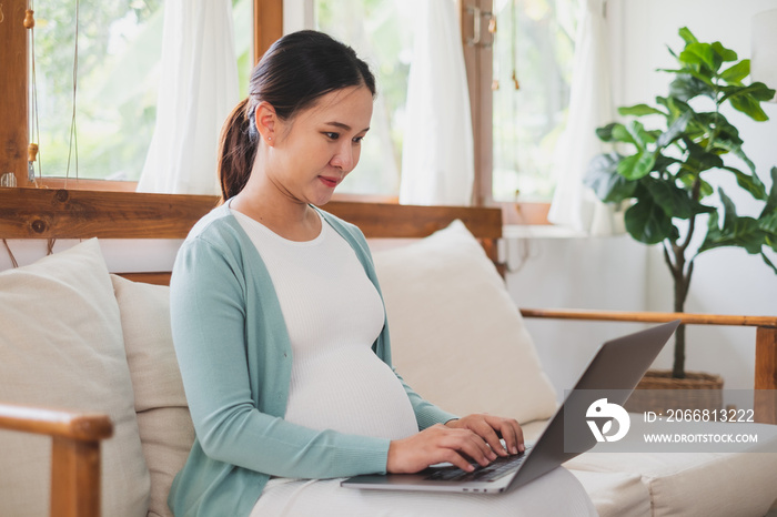 Asian pregnant woman using laptop computer at home