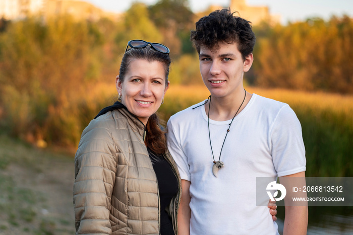 Teenage boy with his mom walking in the autumn park and talking about life and having fun together. The woman gently hugs her almost adult son