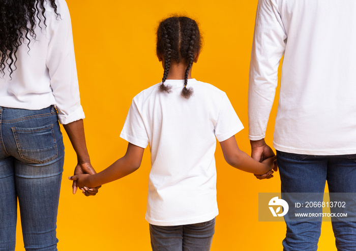 Little afro girl holding hands of her adoptive parents, rear view