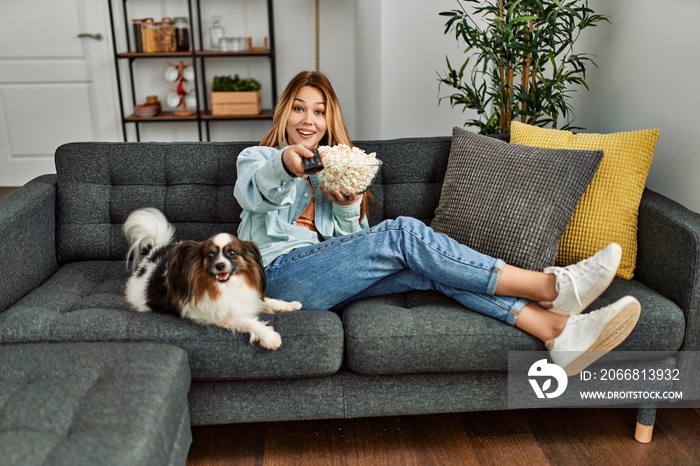 Young caucasian woman watching movie sitting on sofa with dog at home