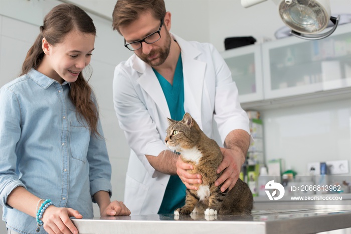 Doctor and girl looking at cat on table in veterinary clinic