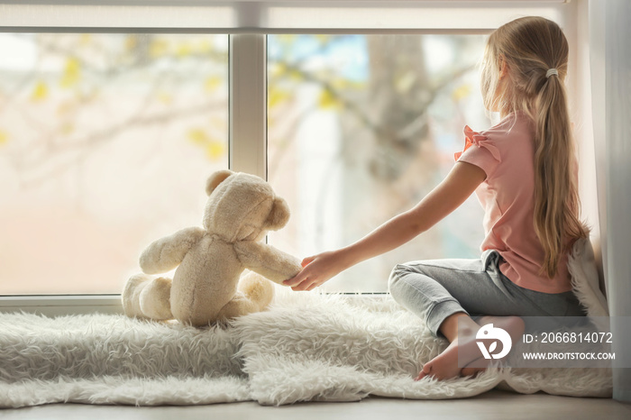 Little girl with teddy bear sitting on window sill. Autism concept