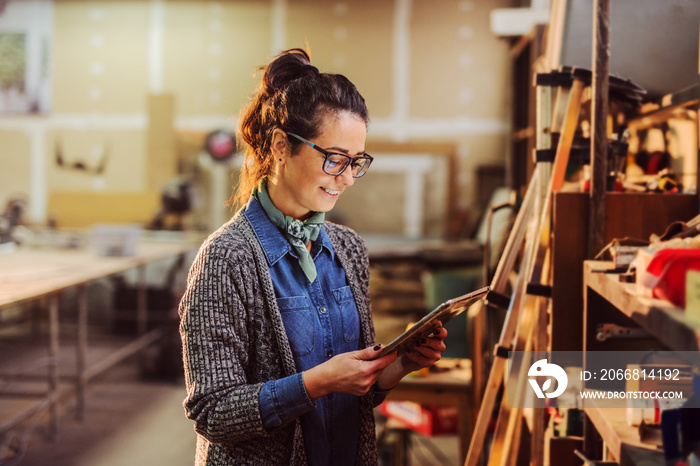 Portrait of beautiful middle age industry female worker holding tablet in her hands and standing in front of shelf with tools.