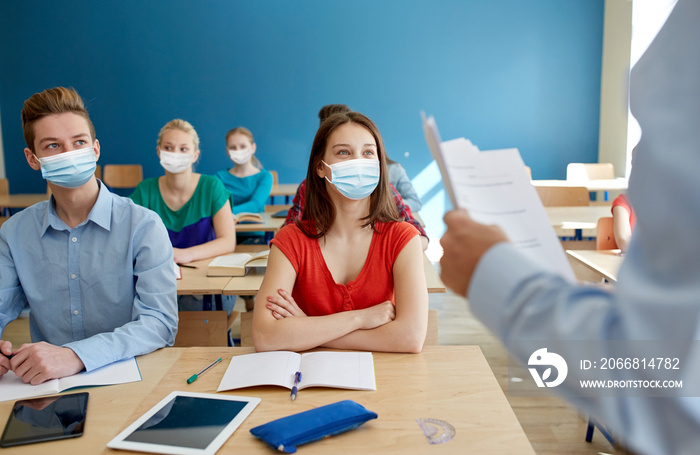 education, healthcare and pandemic concept - group of students wearing face protective medical masks for protection from virus disease and teacher with papers or tests