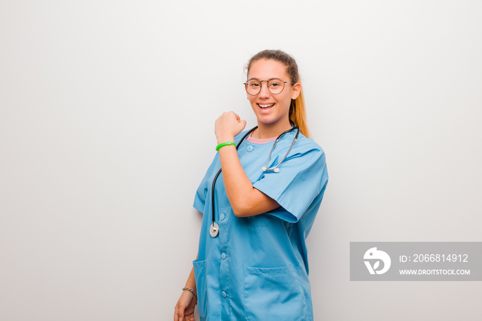 young latin nurse feeling happy, positive and successful, motivated when facing a challenge or celebrating good results against white wall