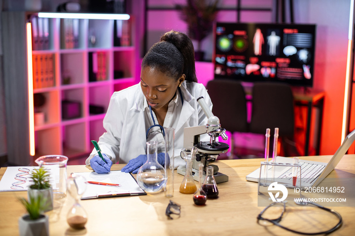 Female african american scientist working in laboratory. Young woman researcher supervisor are doing investigations with test tubes while writing research results.