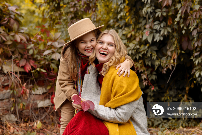 A young adult blonde mother with a 7-year-old daughter on a walk in the autumn park hug and laugh