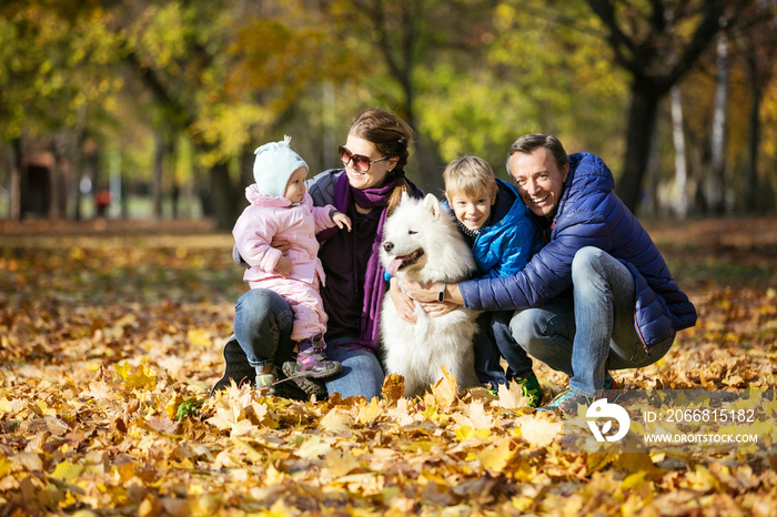 Happy family of four with samoyed dog in autumn park