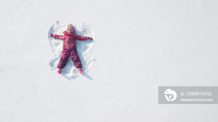 Child girl playing and making a snow angel in the snow. Top flat overhead view