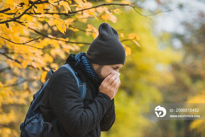 man sneezes and blows his nose in a handkerchief in an autumn park