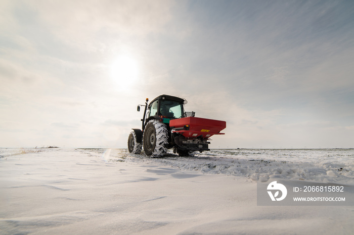 Farmer with tractor seeding - sowing crops at agricultural fields in winter