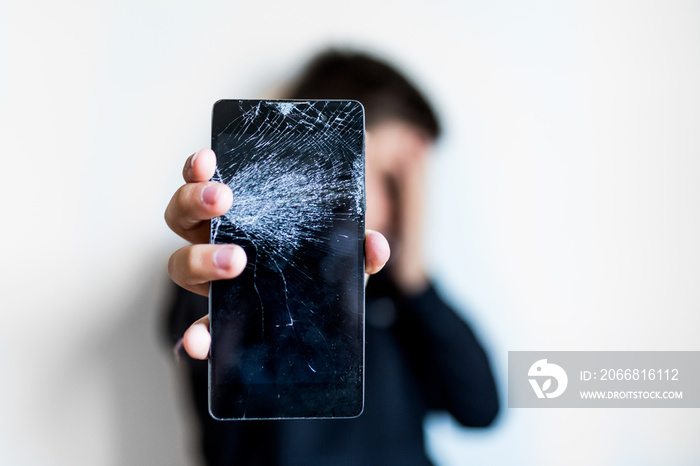 Kid holding broken smartphone covering his face with hand shocked with shame for mistake, expression of fear, scared in silence, secret concept