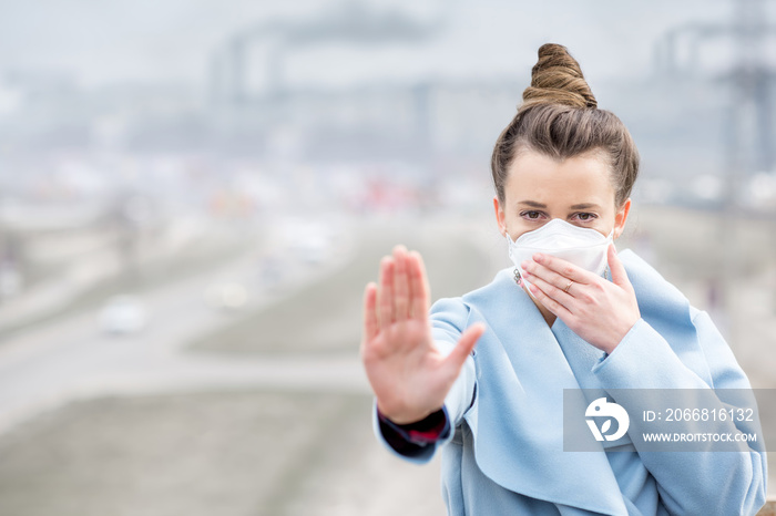 Young woman in protective mask feeling bad in the city with air pollution from traffic and manufacturing. Smog concept