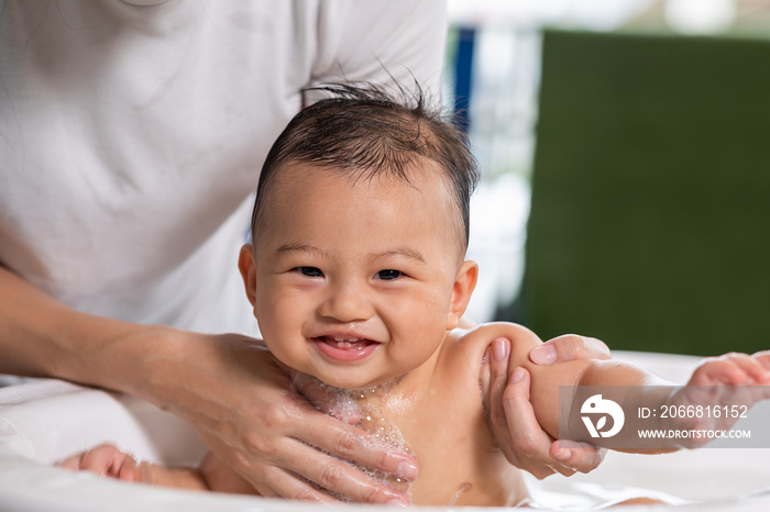 Cheerful of asian newborn baby enjoying bathing in bathtub. mother bathing her son in warm water. Happy adorable newborn infant smile in tub relax and comfortable. Newborn baby care concept