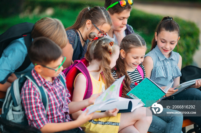 Happy Schoolmates Portrait. Schoolmates seating with books in a wooden bench in a city park and studying on sunny day.