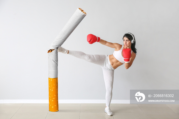 Sporty female boxer kicking cigarette near light wall