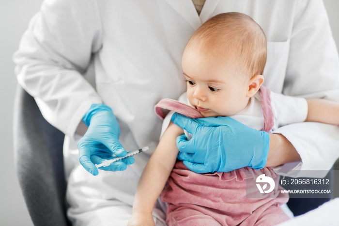 medicine, healthcare and vaccination concept - female pediatrician doctor or nurse with syringe making injection of vaccine for baby girl patient at clinic or hospital