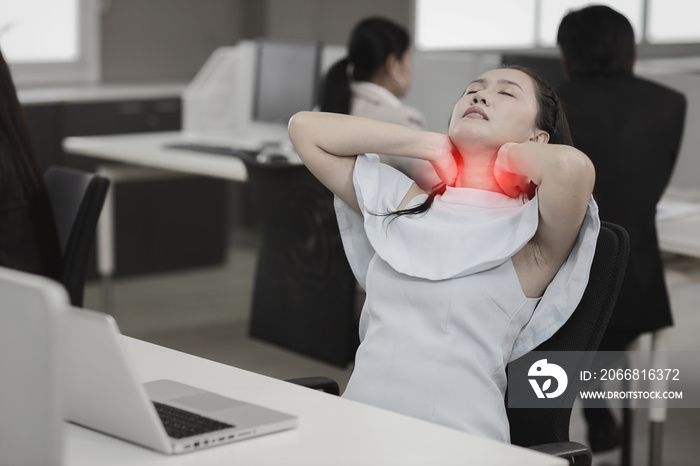 Mid adult asian stressed businesswoman sitting and holding her neck pain or having problem with part of body backache after working on computer too long time in office. Office syndrome concept