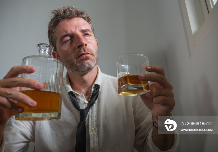 portrait of 30s to 40s alcoholic  man in lose necktie drinking desperate holding whiskey glass thoughtful drunk and depressed completely wasted in alcohol addiction concept