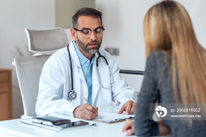 Shot of handsome mature male doctor talking while explaining medical treatment to patient in the consultation.