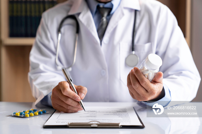 male medicine doctor hand holds the bottle of pills and writes a prescription to the patient at the worktable. Panacea and life save, prescribing treatment legal drug store concept.