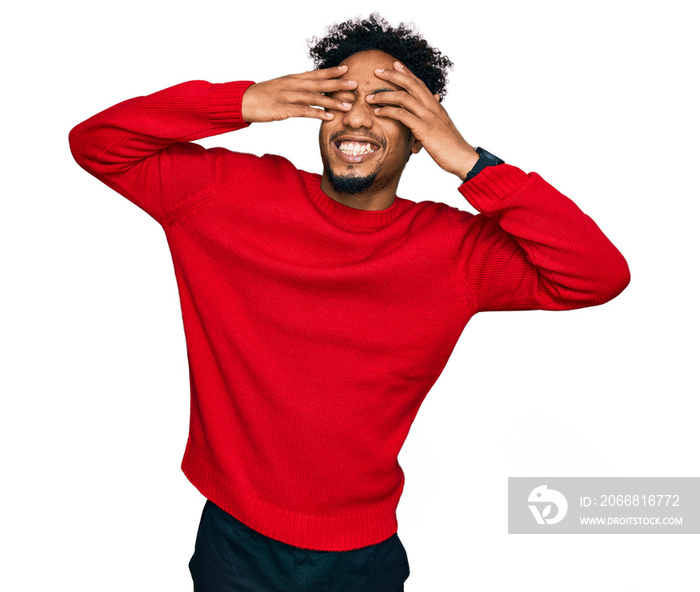 Young african american man with beard wearing casual winter sweater covering eyes with hands smiling cheerful and funny. blind concept.