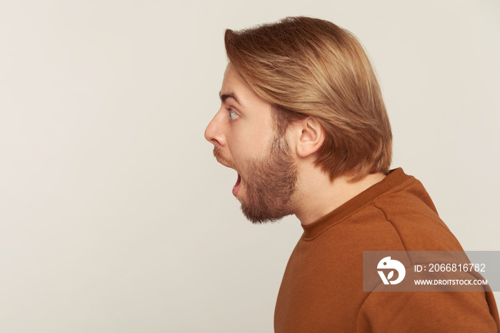 Closeup profile of surprised bearded man screaming in sudden fright and shock, looking to side copy space with astonished expression, open mouth in amazement. studio shot isolated on gray background