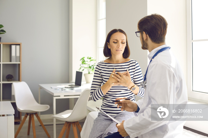 Visiting hospital. Worried middle-aged female patient, touching her chest, explains symptoms to her doctor and complains of heart pain. Concept of care for heart attack and cardiovascular disease.