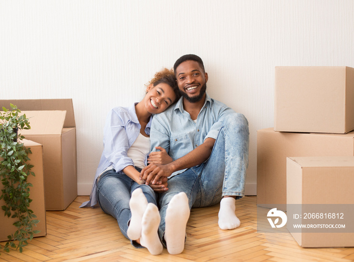 Couple Sitting On Floor Among Moving Boxes In New House