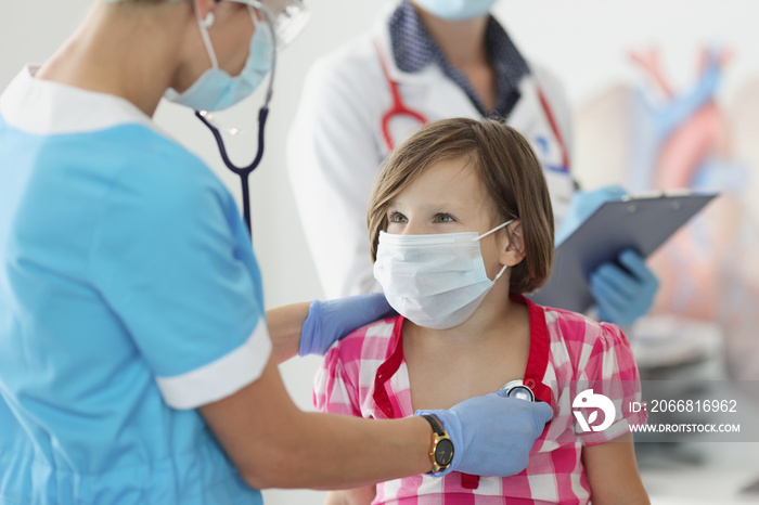 Pediatrician doctor listening with stethoscope to little girl in clinic