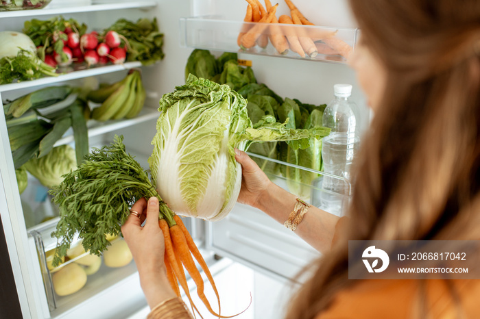 Woman taking fresh cabbage and carrot from the refrigerator at home, close-up view