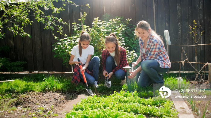 Photo of young mother with daughters sitting at garden and taking care of garden bed