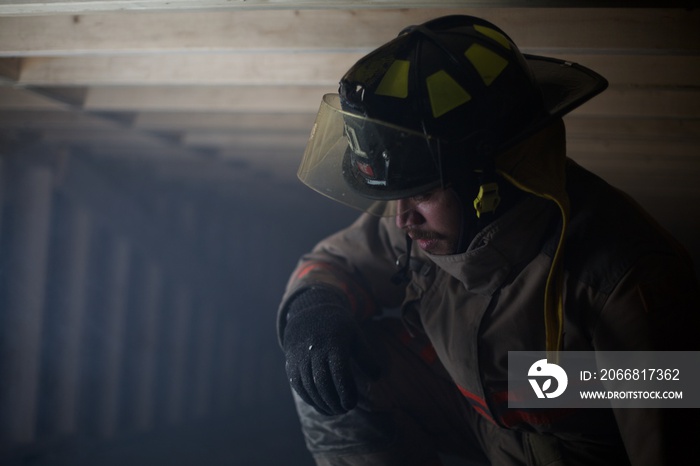 Fire Fighter kneeling down in wooden structure filled with smoke