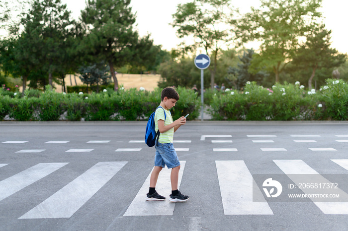 Boy looks at their mobile phones while crossing a crosswalk on the street. Concept of mobile phone addiction