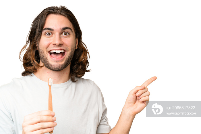 Young handsome man brushing teeth over isolated background surprised and pointing finger to the side