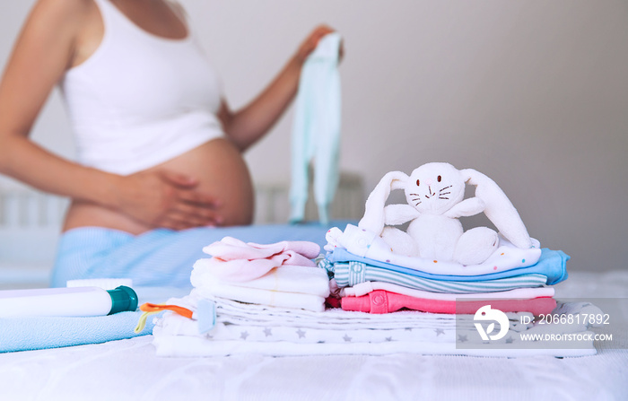 Pile of baby clothes, stuff and pregnant woman in home interior