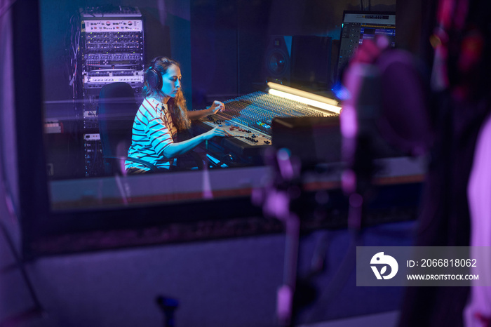 Young musical producer using music keyboard to record a song for singer in the recording room