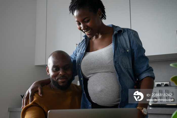 Man and pregnant woman looking at laptop in kitchen