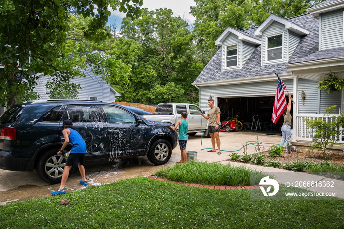 Air Force service member washes his vehicles with his sons in the driveway.