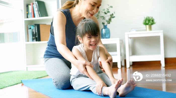 Asian mother teaching her daughter and practicing light yoga exercise stretching movements on a mat learning to control various parts of the body in the brightly lit sunny morning living room. Concept