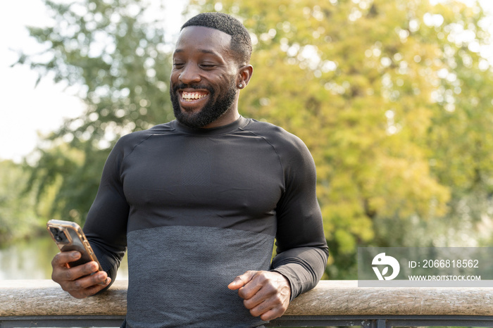 Smiling athletic man looking at smart phone on footbridge in park