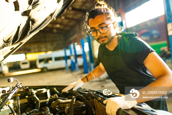 indian man auto mechanic working indoors in car shop